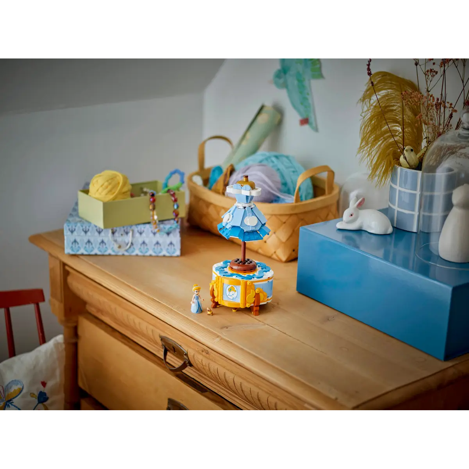 A wooden dresser hosts a dress-shaped music box, Cinderella figurine, yarn, and decor.