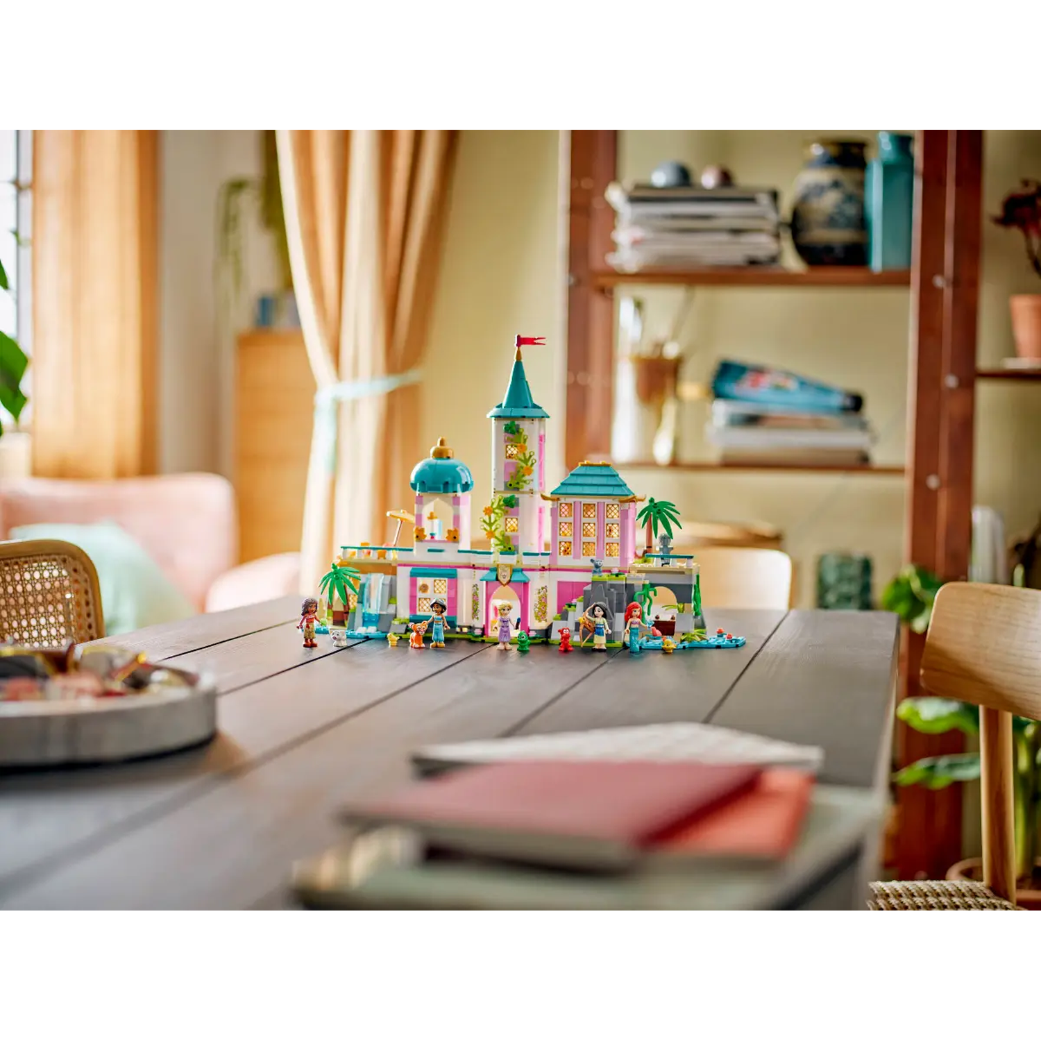 Een Lego kasteel staat op een houten tafel. Figuren staan rond het kasteel. Achtergrond bevat een houten plank, gordijnen en een stoel.