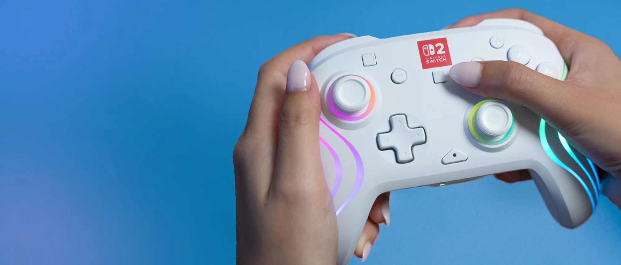 Mains tenant une manette Nintendo Switch blanche, sur fond dégradé bleu. La manette a des lumières et des boutons lumineux.