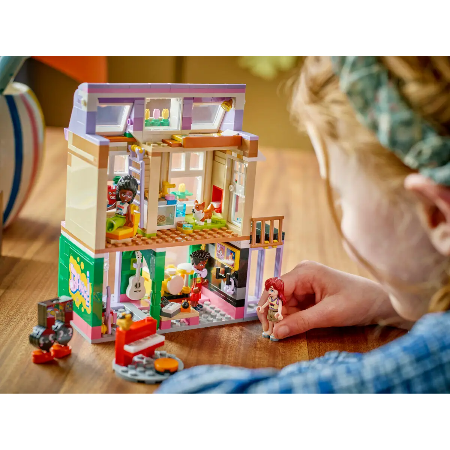 A child is playing with a Lego Friends set, a two-story building with figures and musical instruments.