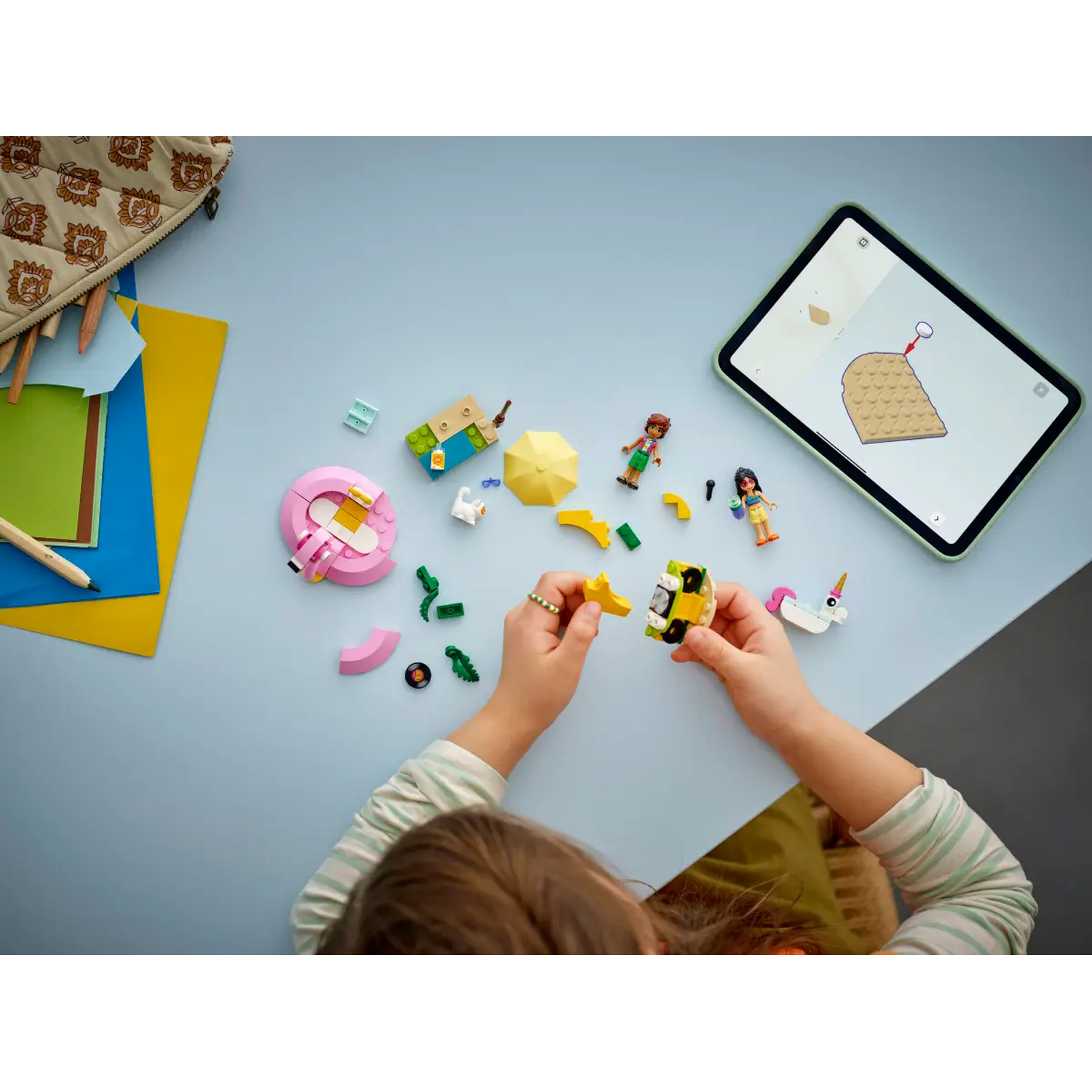 A child is playing with toy blocks, a tablet showing instructions, and other toys on a blue and gray surface.