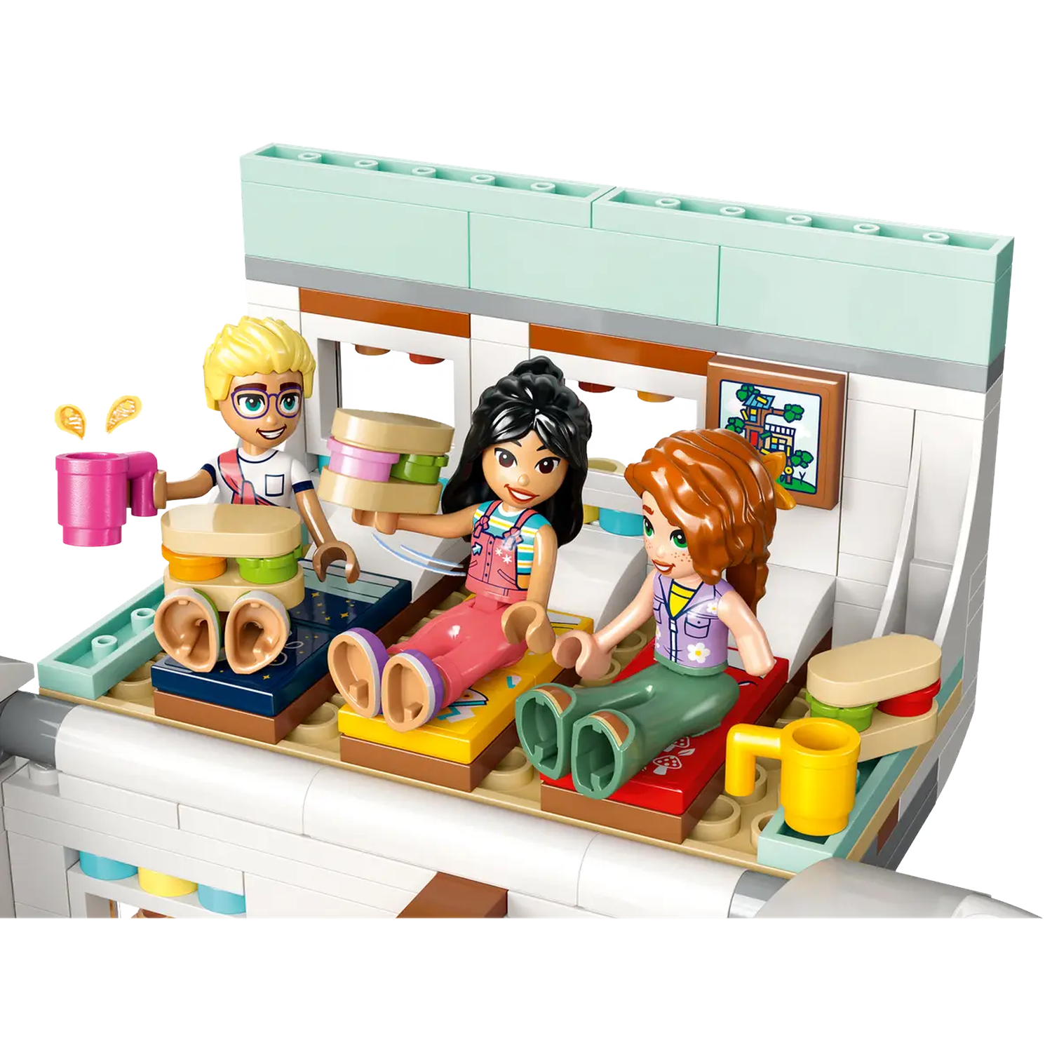 Drie Lego-figuren zitten in een trein, met eten en drinken. Een schilderij hangt aan de muur.