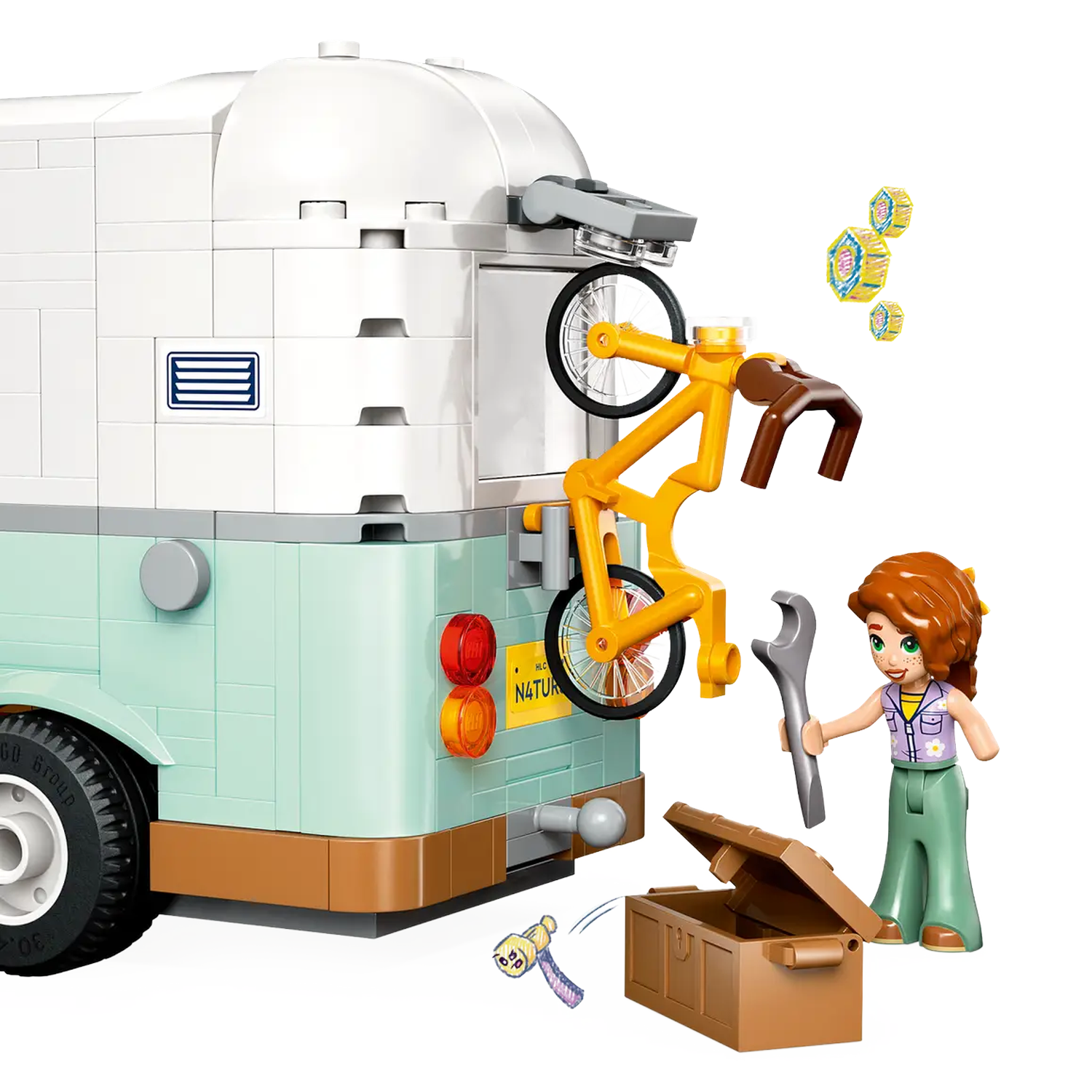 Een Lego-scène toont een busje met een fiets, een figuur met een moersleutel en een gereedschapskist. Accessoires zweven in de buurt.