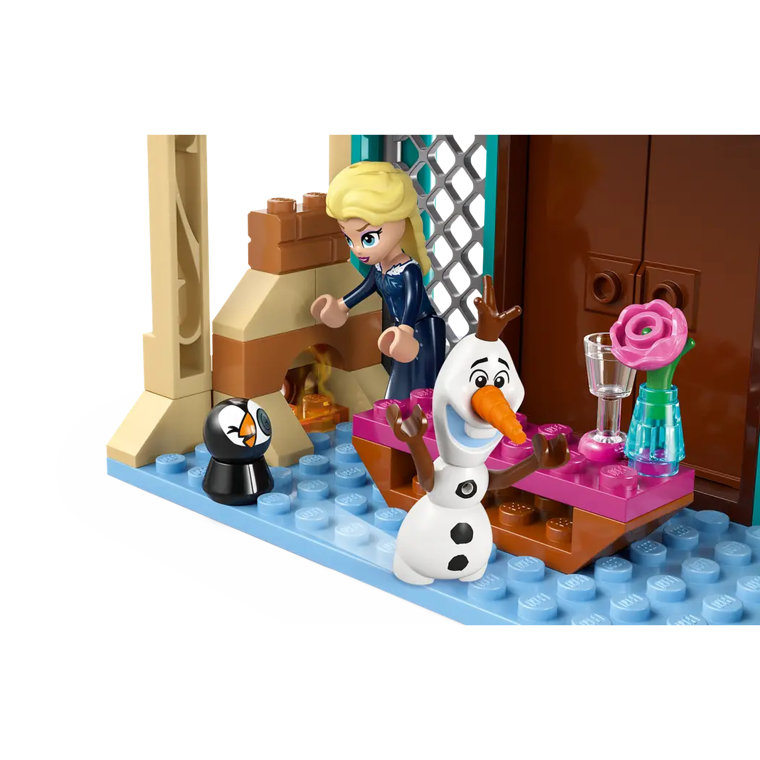 Lego scene with Elsa, Olaf, and a penguin. Elsa stands near a fireplace. Olaf has a carrot nose. A pink rose decorates a table.