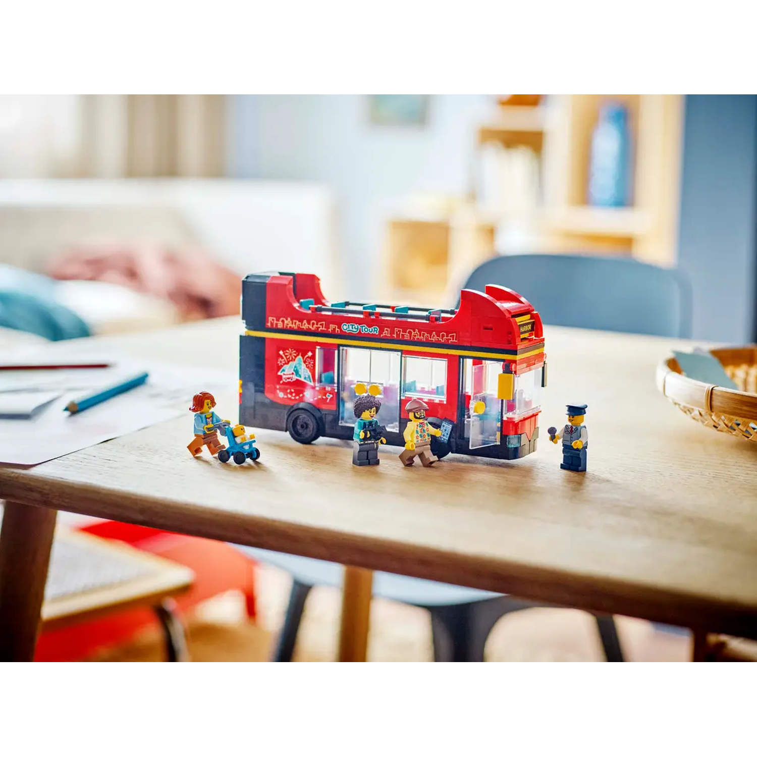 A Lego City Tour bus with passengers and figures on a wooden table. A woman pushes a baby carriage.