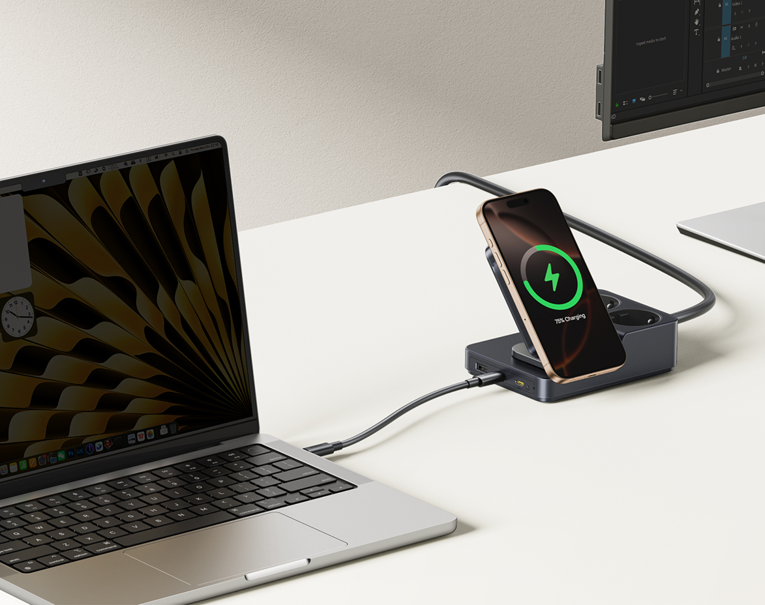 Una laptop, un teléfono cargando y un monitor en un escritorio blanco. El teléfono muestra un 75% de carga. La laptop está conectada.