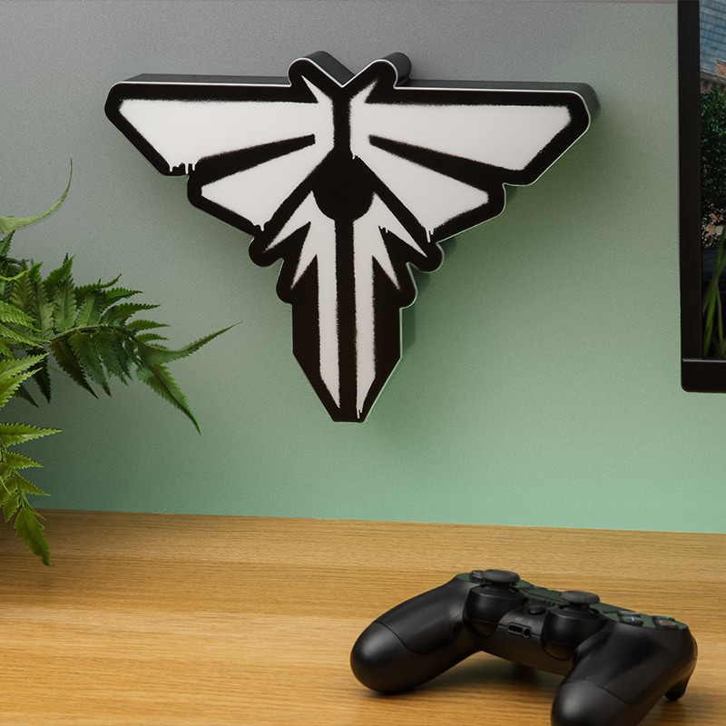 Un logo de Firefly blanco y negro en una pared menta, un mando, una mesa de madera y un helecho. Una pantalla es visible en el fondo.