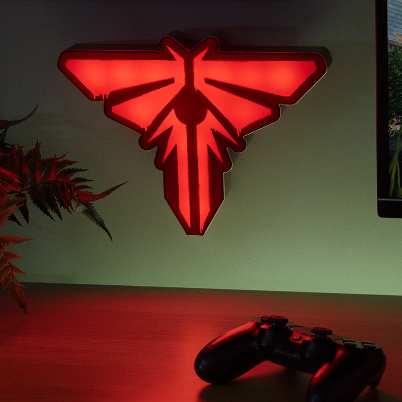 Lámpara con el logo de Firefly roja en la pared, mando en el escritorio. Helecho a la izquierda. TV a la derecha. Combinación de colores rojo y negro.