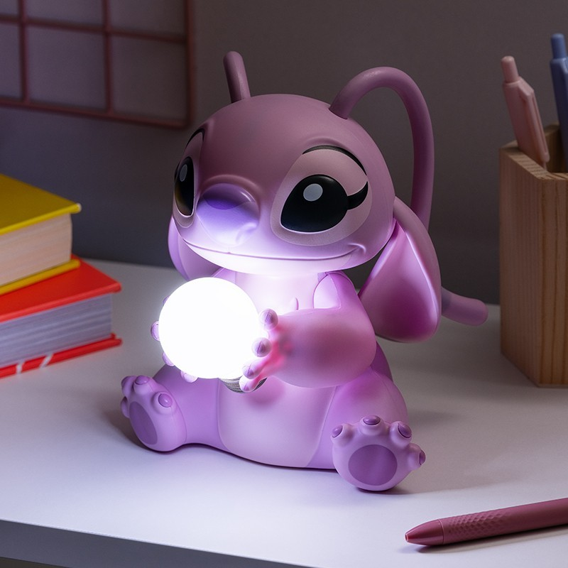 Una lámpara rosa de Angel sostiene un orbe brillante. Libros, bolígrafos y un portalápices están en el fondo, todo sobre un escritorio blanco.