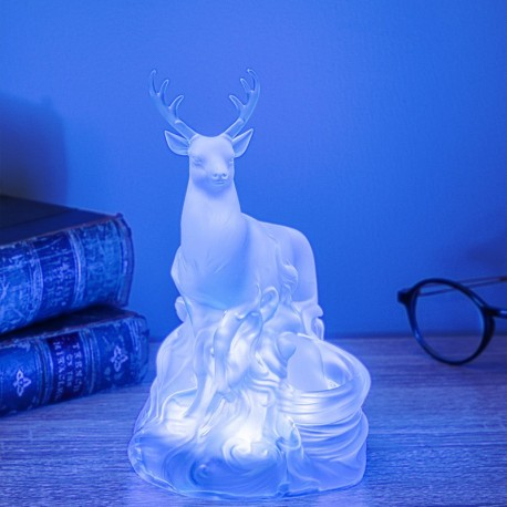 Una estatua de ciervo brillante con grandes cuernos sobre una mesa. Libros y gafas en el fondo, todo iluminado con luz azul.