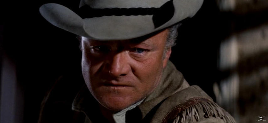 Nahaufnahme eines Mannes mit Cowboyhut. Er hat einen strengen Blick und schaut den Betrachter direkt an. Der Hintergrund ist dunkel.