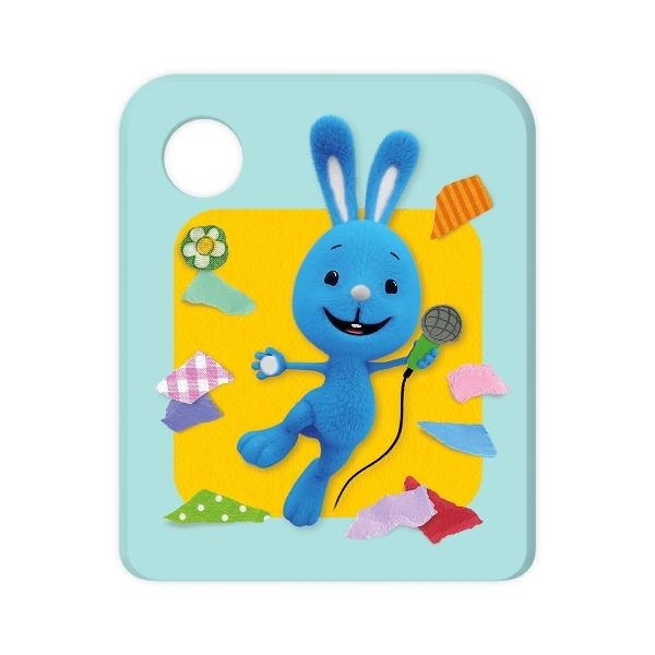 Ein blaues Kaninchen mit Mikrofon. Es steht auf gelbem Grund, umgeben von bunten Stoffresten, auf blauem Hintergrund.