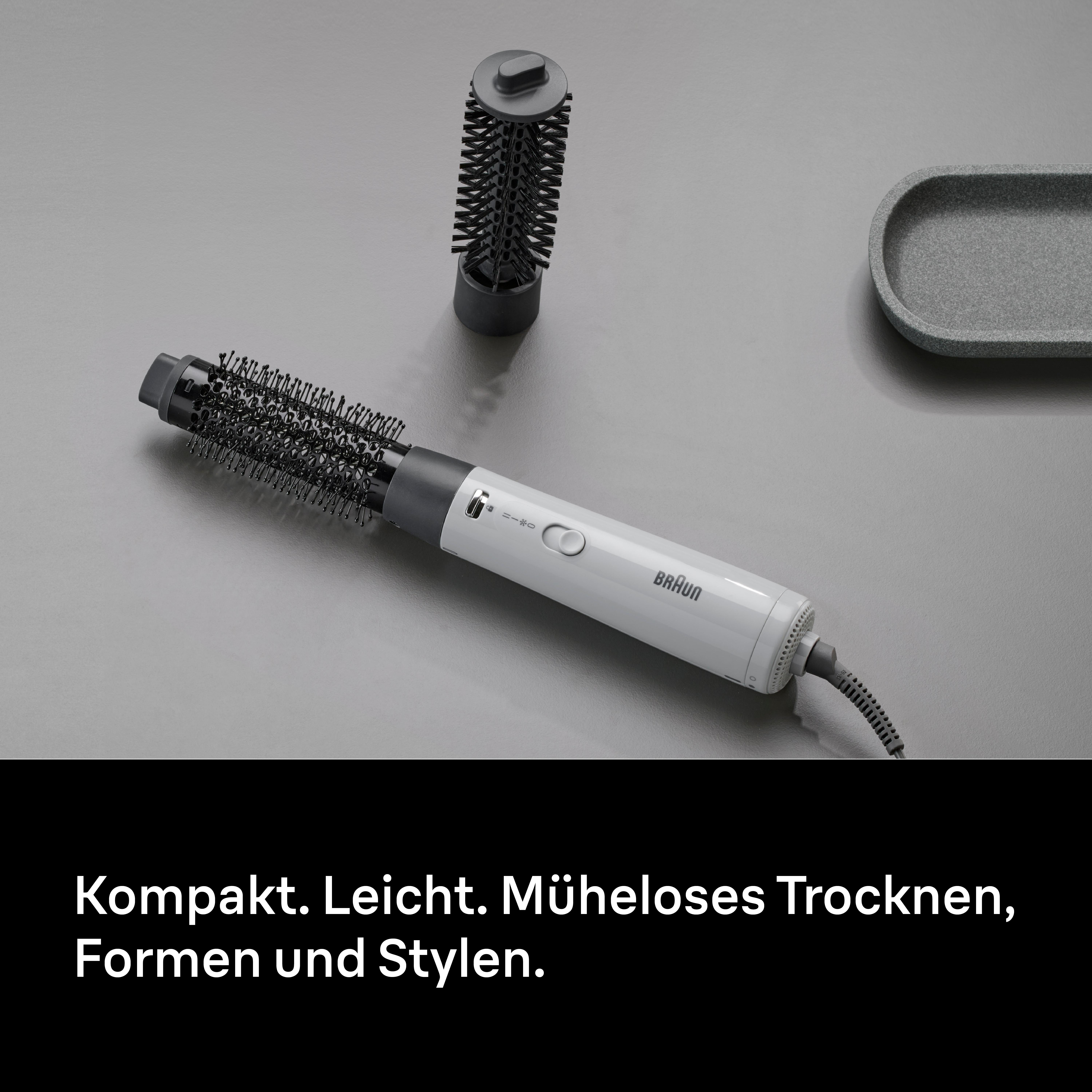 Ein weiß-schwarzes Braun-Haarstylinggerät mit zwei Aufsätzen auf grauer Oberfläche mit grauer Ablage.