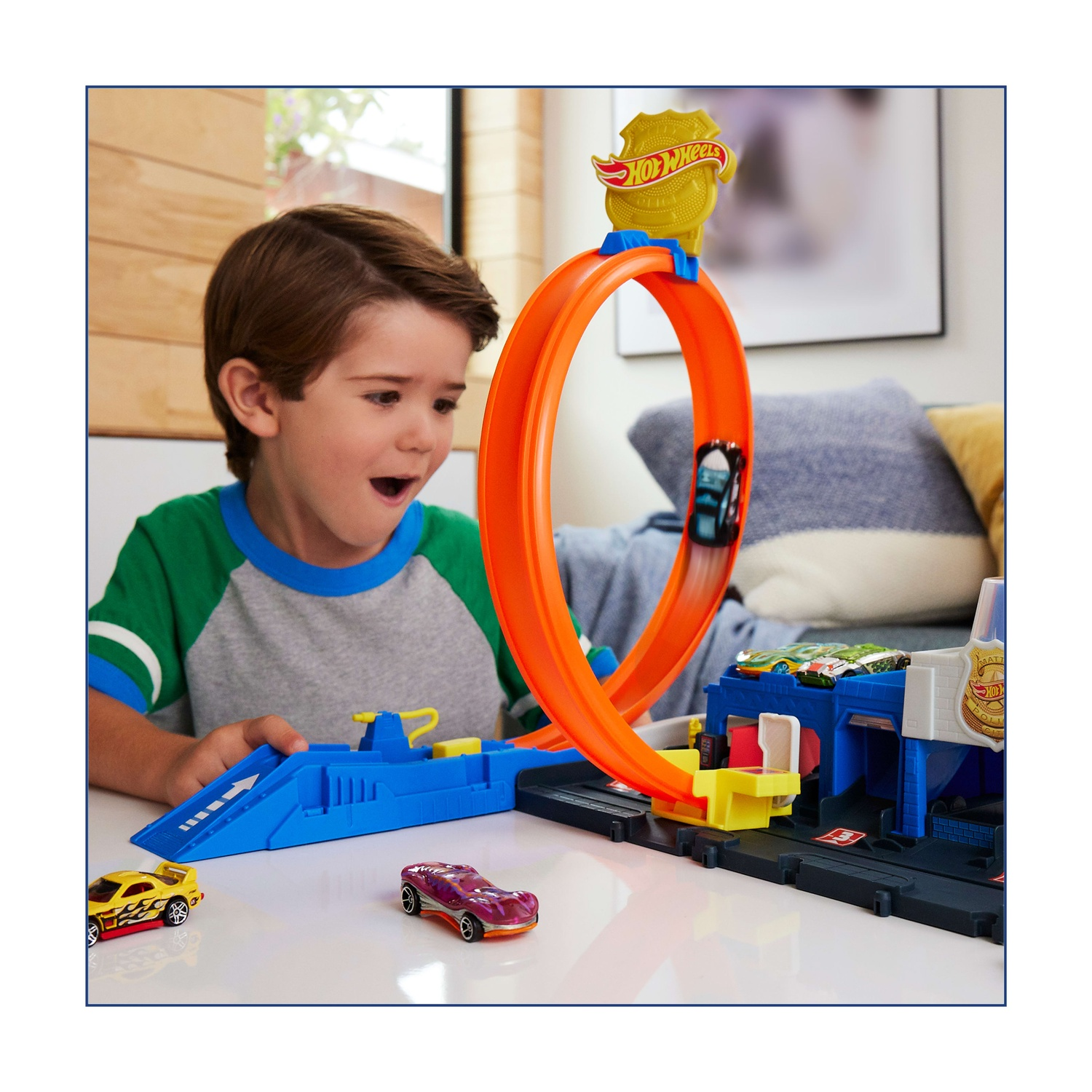 Un bambino guarda le macchinine Hot Wheels su una pista. La pista comprende un'ansa e un garage con macchinine.