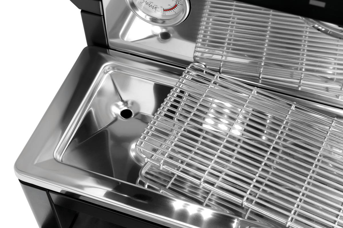 Nahaufnahme eines Edelstahlgrills mit Thermometer. Ein Metallrost befindet sich in einem Becken und reflektiert das Licht.