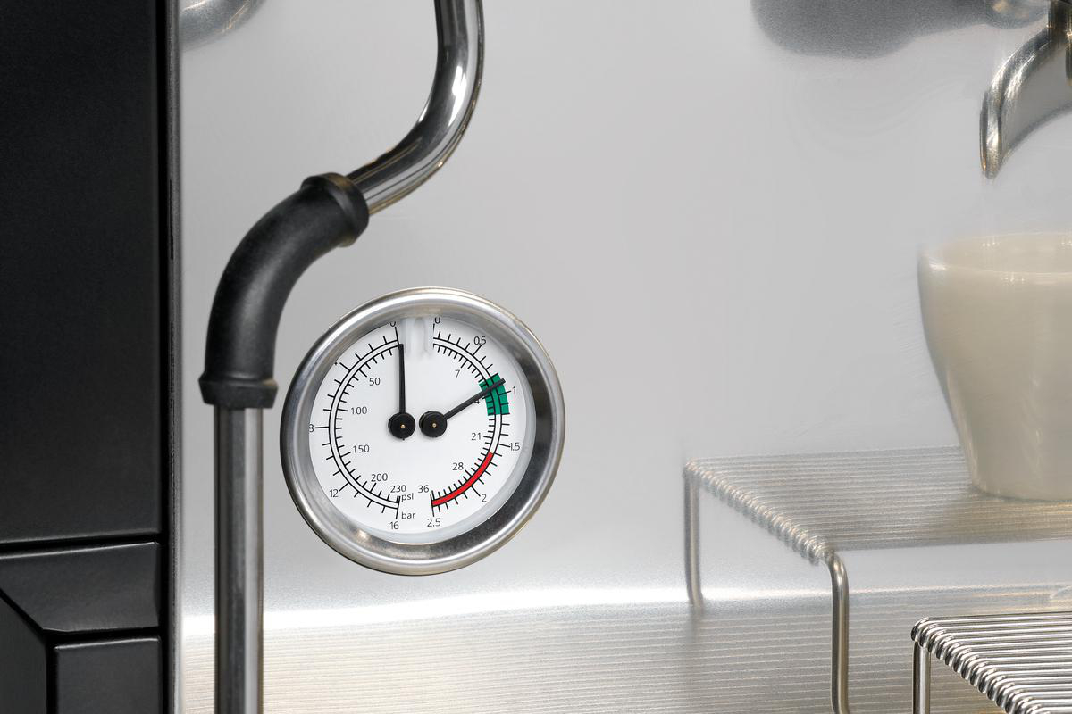 Nahaufnahme einer Kaffeemaschine mit Manometer, Tasse und Metalldetails, die die Funktionalität und das Design zeigen.