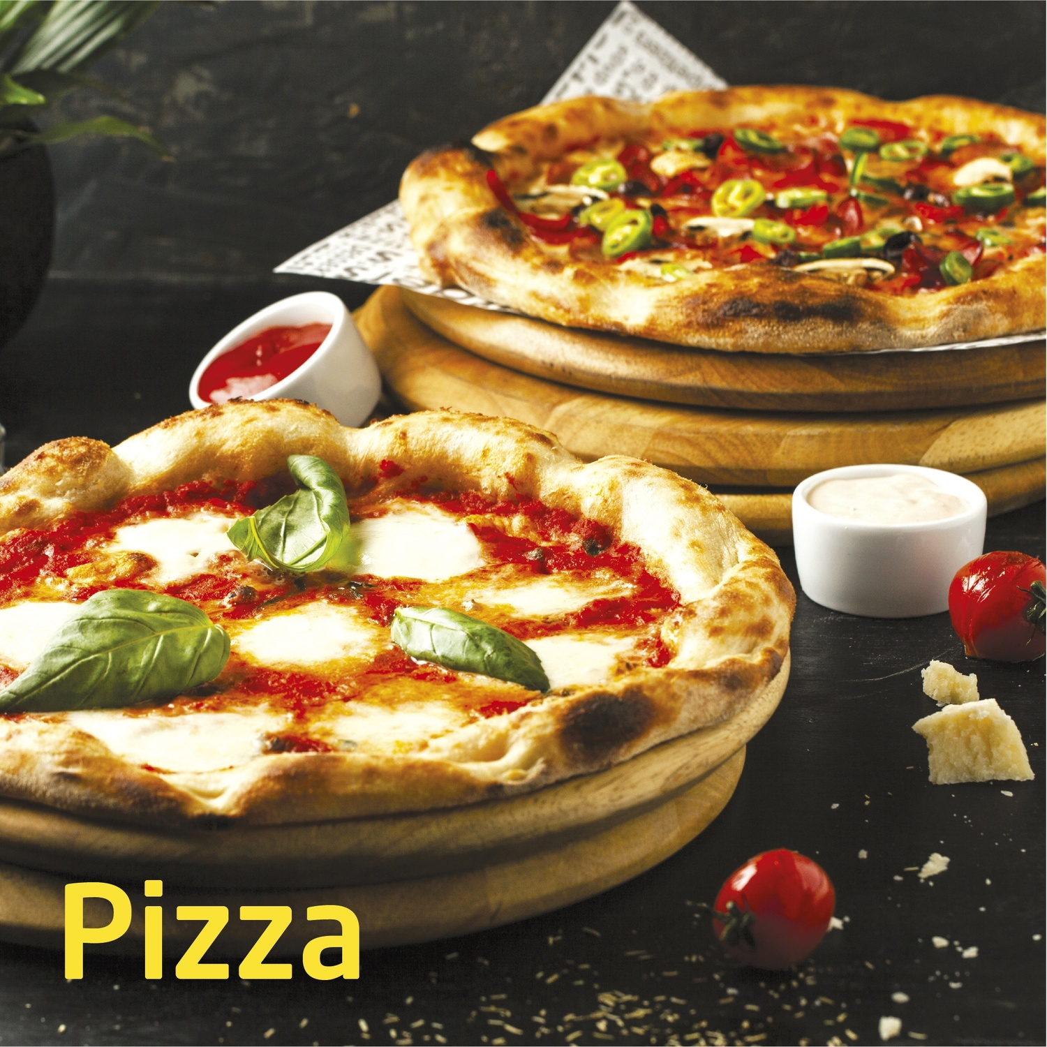 Due pizze su assi di legno. Una con mozzarella e basilico, l'altra con verdure. Pomodori, formaggio e salse sono sul tavolo.