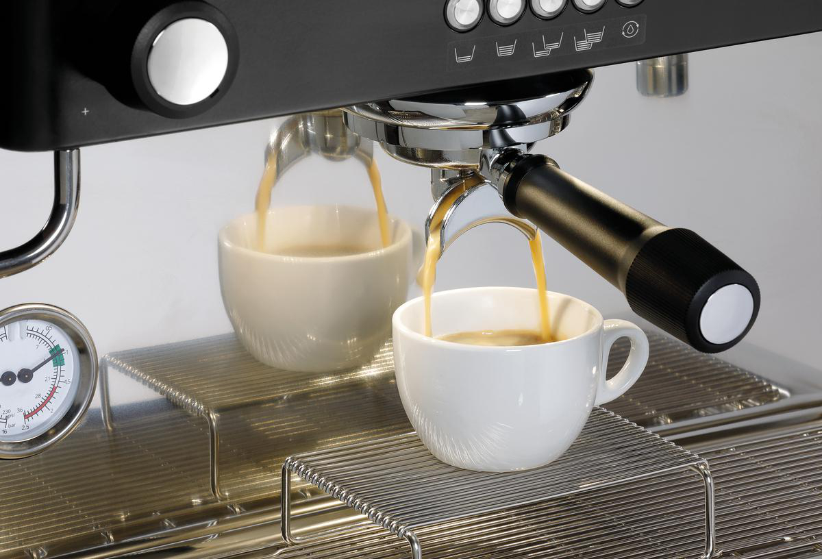 Espressomaschine, die Kaffee in zwei weiße Tassen ausgibt. Eine Anzeige und Bedienelemente sind sichtbar. Die Maschine ist schwarz und silber.