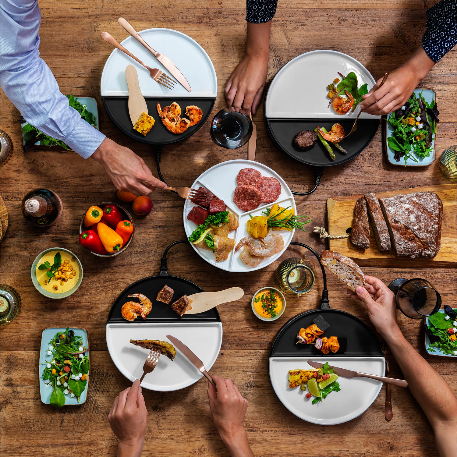 Overzichtsfoto van een maaltijd met verschillende borden, gerechten en handen die naar eten op een houten tafel grijpen.
