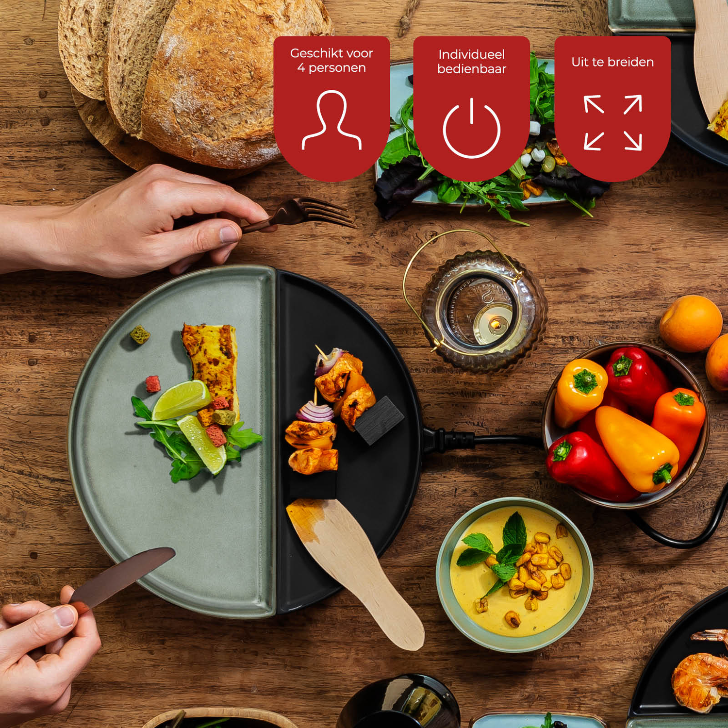 Een houten tafel met eten, waaronder brood, borden met eten, groenten en een kom soep. Handen houden bestek vast.