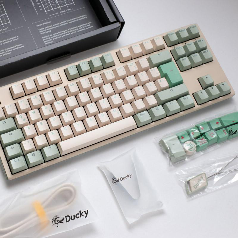 Eine beige und mintfarbene mechanische Tastatur mit zusätzlichen Tastenkappen, Kabeln und Zubehör der Marke Ducky.