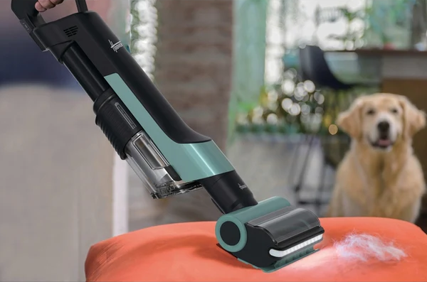 Un aspirapolvere sta pulendo un cuscino rosso con peli di cane. Un cane golden retriever è sullo sfondo.