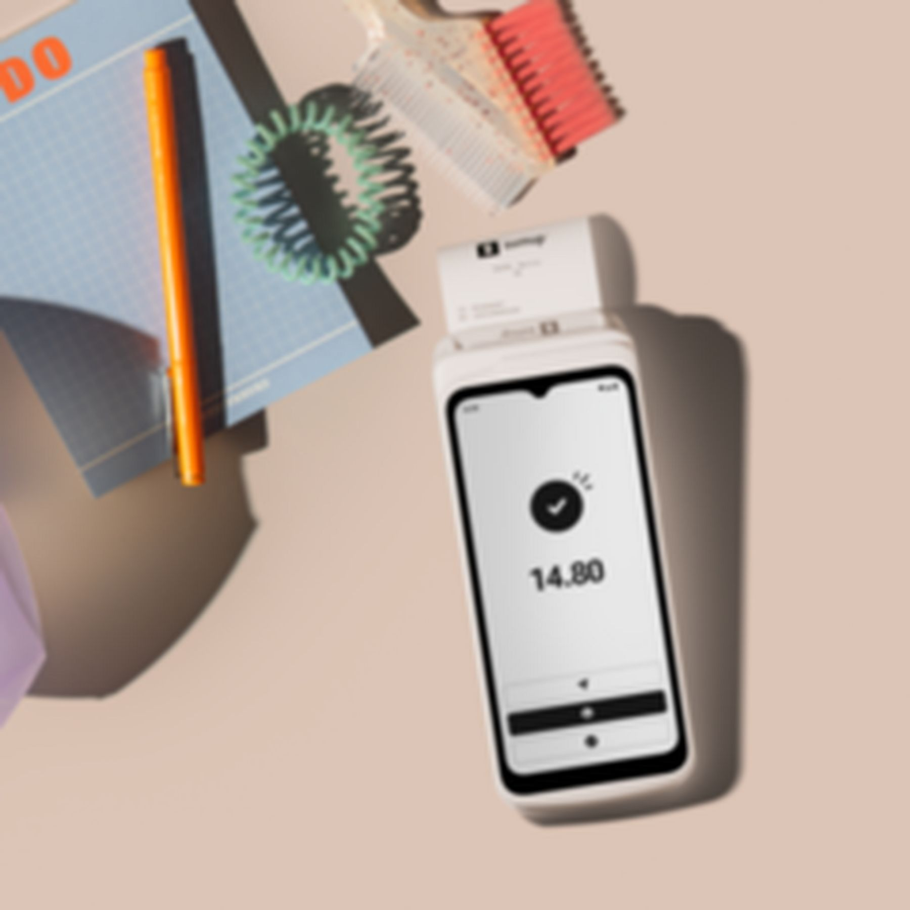 Un smartphone affichant 14,80 est à côté d'un bloc-notes, d'un stylo, d'un élastique et d'une brosse.