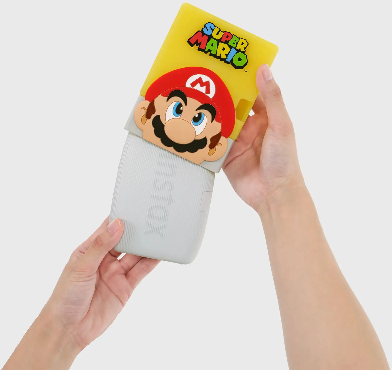 Hände halten eine gelbe und graue Super Mario Instax Kamerahülle. Marios Gesicht ist auf der Hülle.
