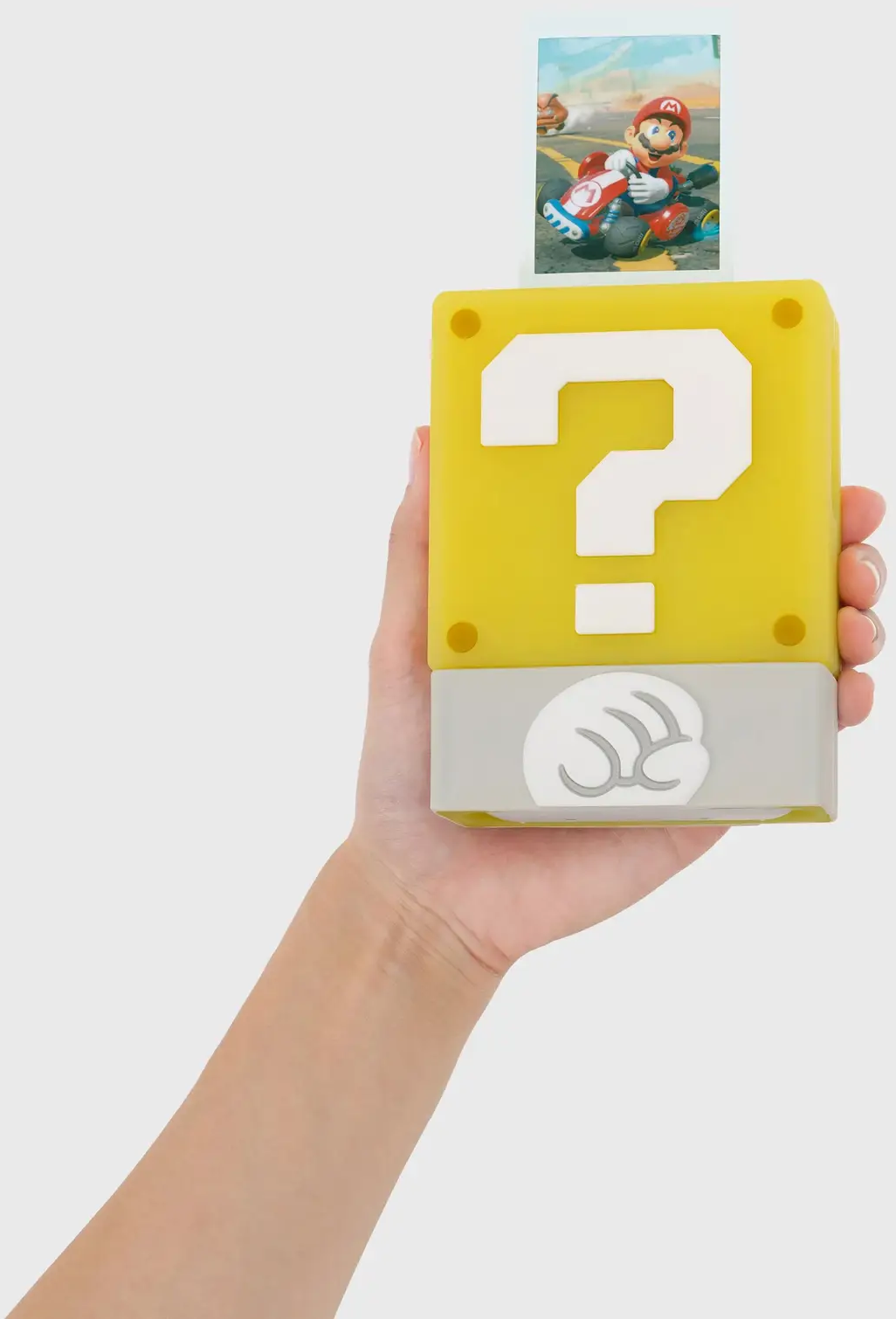 Eine Hand hält einen gelben Fragezeichenblock mit einem Bild von Mario in einem Kart. Der Hintergrund ist weiß.