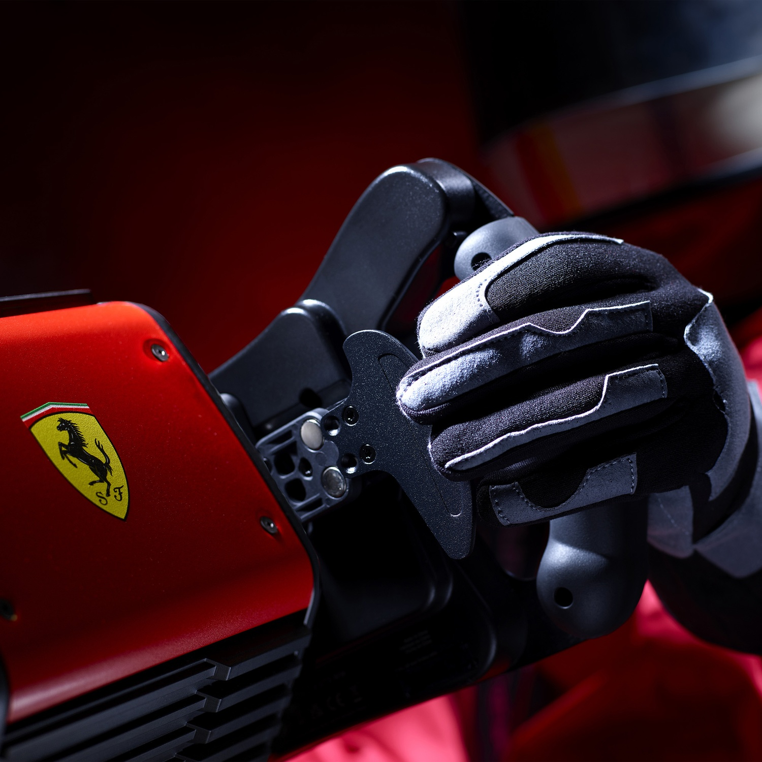Une main gantée saisit une commande noire. Un appareil rouge avec le logo Ferrari est à gauche. Le fond est un dégradé de rouge.