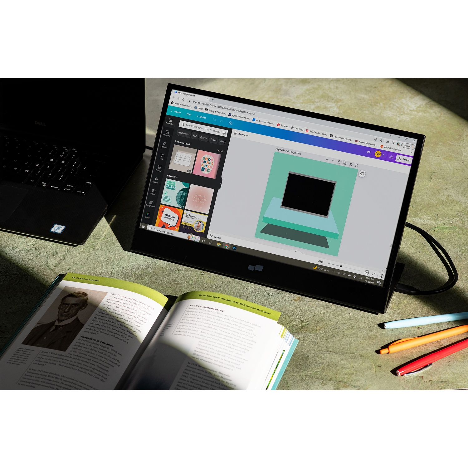 Laptop, opened book, and a tablet showing a design on a green surface. Pens are on the right.