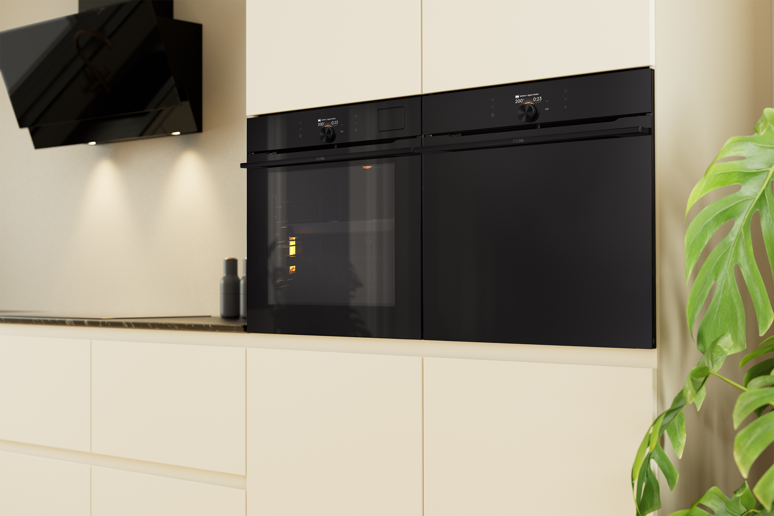 A modern kitchen with black ovens, a range hood, and a green plant. Cream cabinets and a countertop are also visible.