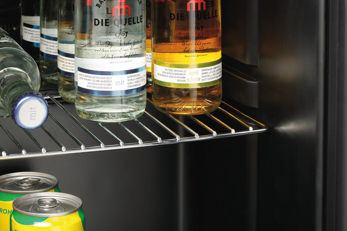 Im Kühlschrank stehen Flaschen und Dosen auf Regalen. Etiketten sind sichtbar. Der Hintergrund ist schwarz.