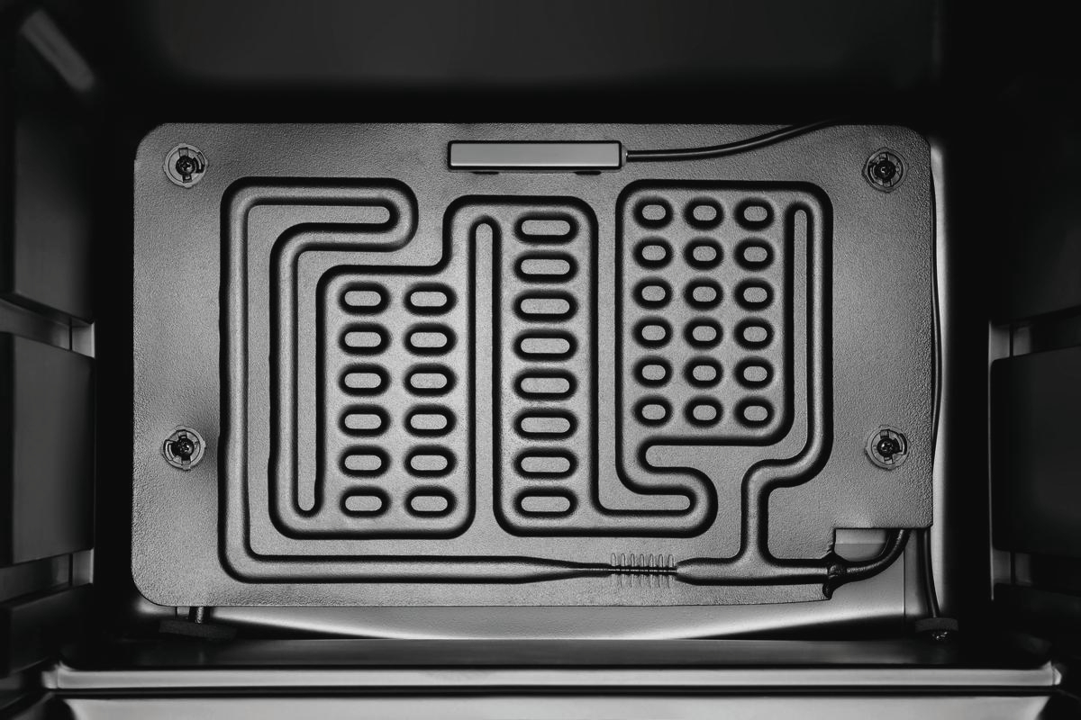 Im Inneren eines schwarzen Ofens. Eine rechteckige, gemusterte Metallplatte mit mehreren Lochreihen ist sichtbar. Sie hat ein metallisches Kabel.