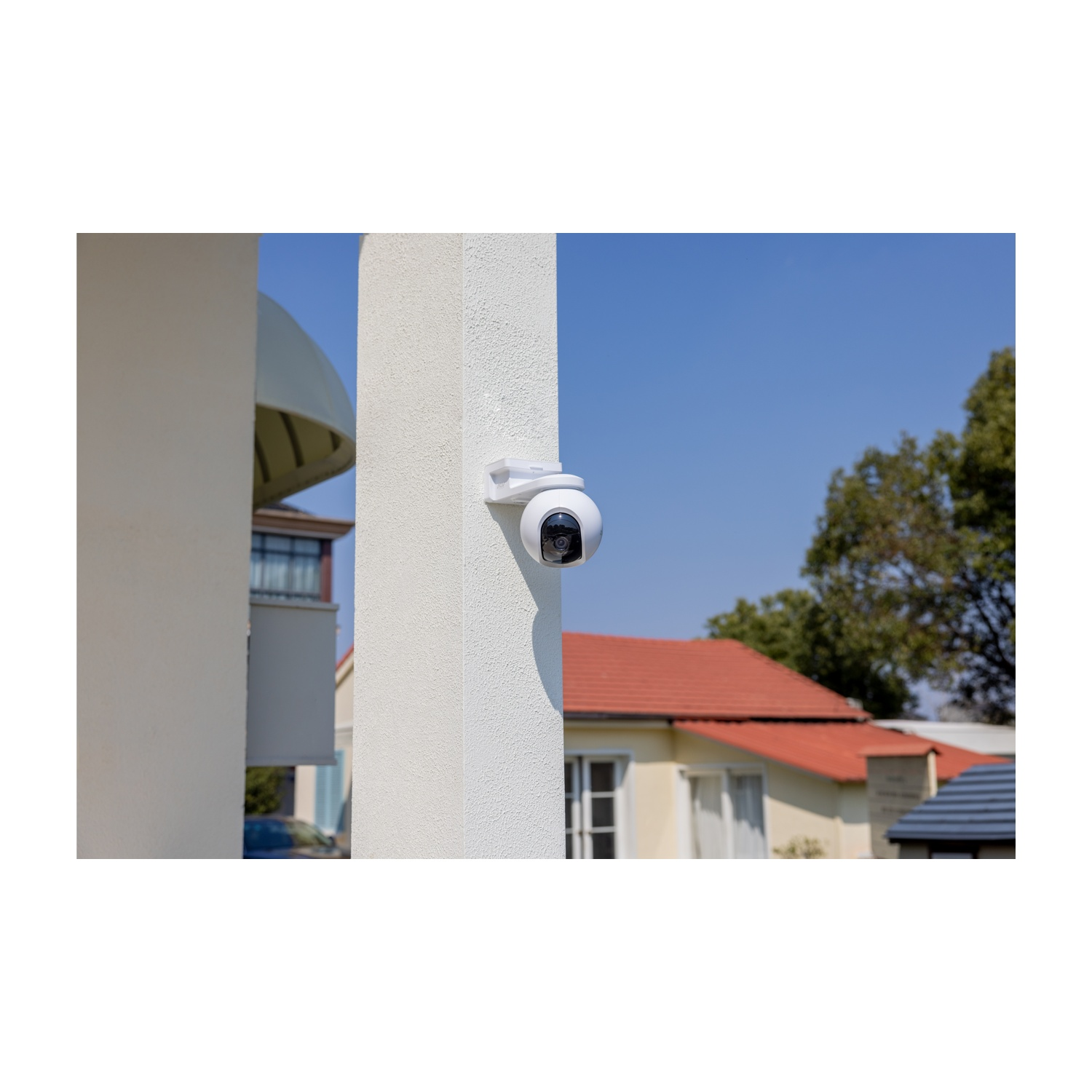 Una telecamera di sicurezza è montata su un pilastro bianco. Case con tetti rossi e cielo blu sullo sfondo.