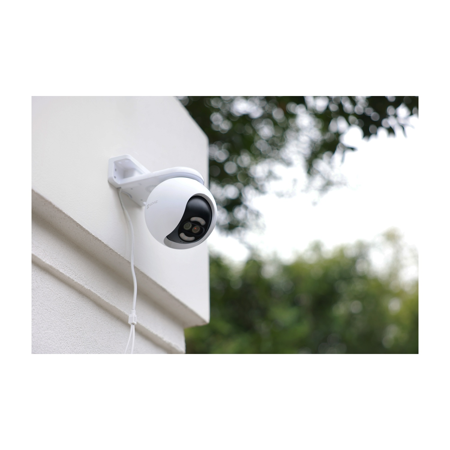 Una telecamera di sicurezza bianca montata su un muro bianco. La telecamera ha un obiettivo nero e un cavo bianco penzolante.