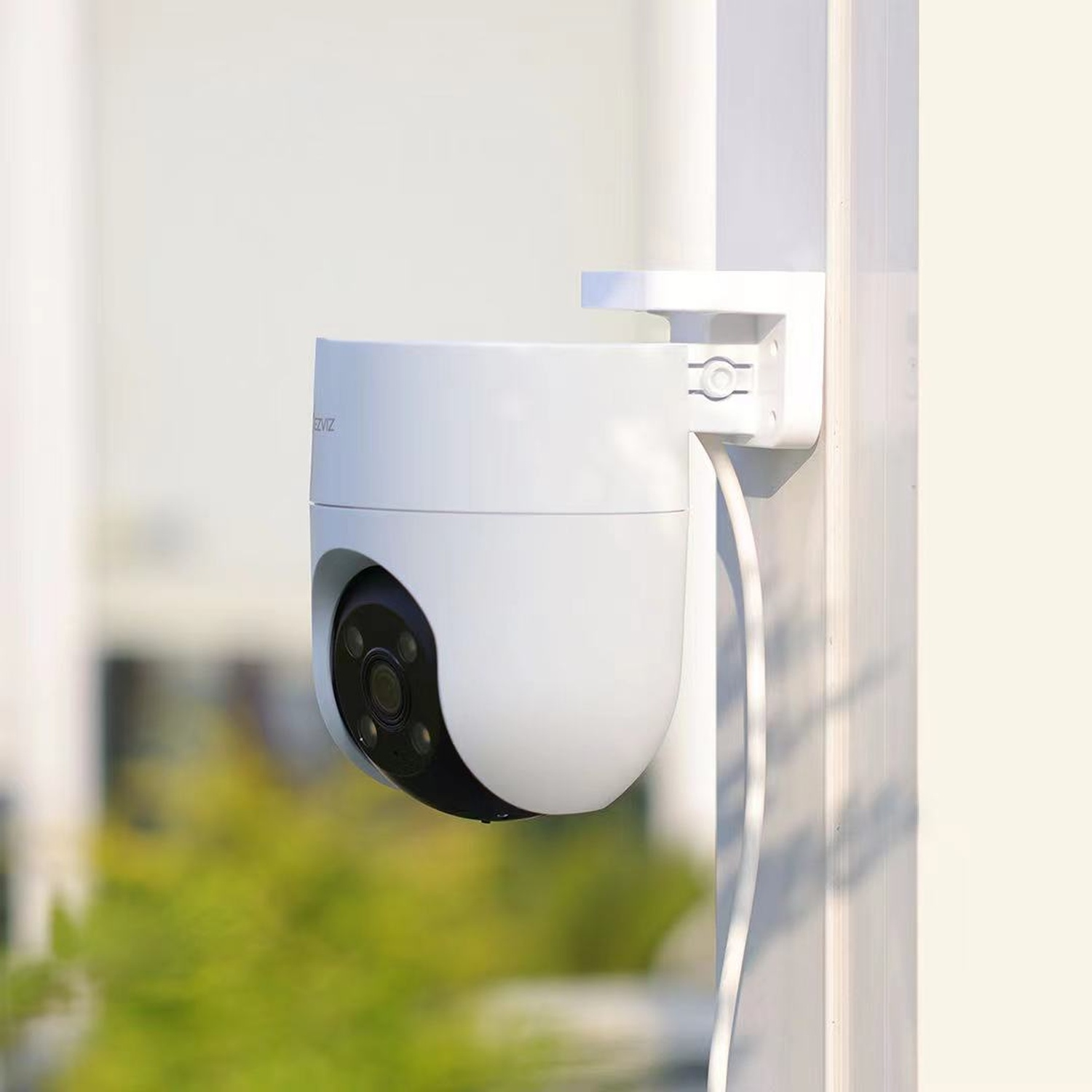 Una telecamera di sicurezza bianca montata su un palo bianco. La telecamera ha un obiettivo nero ed è circondata da vegetazione verde.