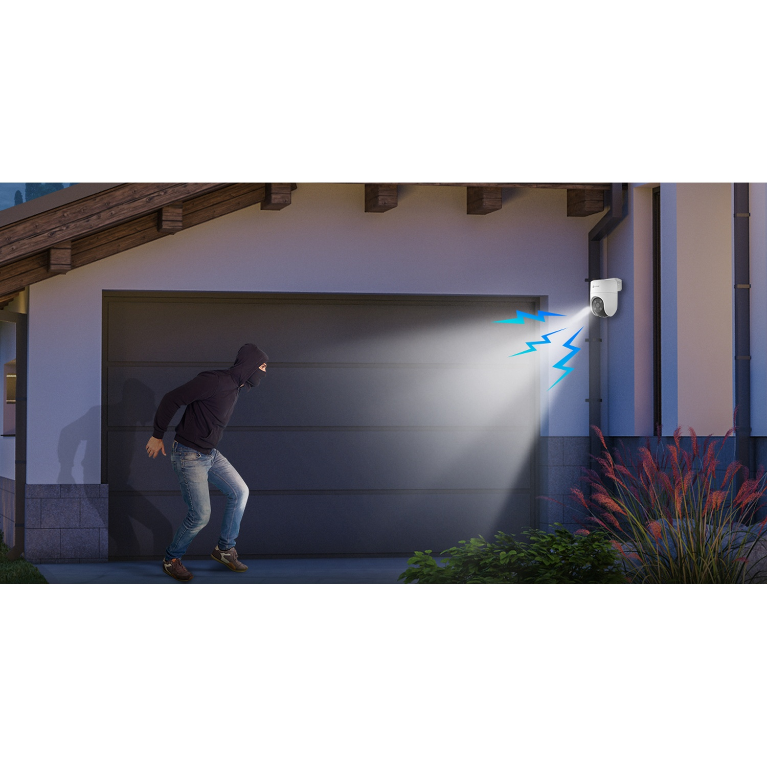 Un ladro in nero è illuminato da una telecamera di sicurezza. La telecamera è montata su un edificio. Un portone del garage è dietro il ladro.