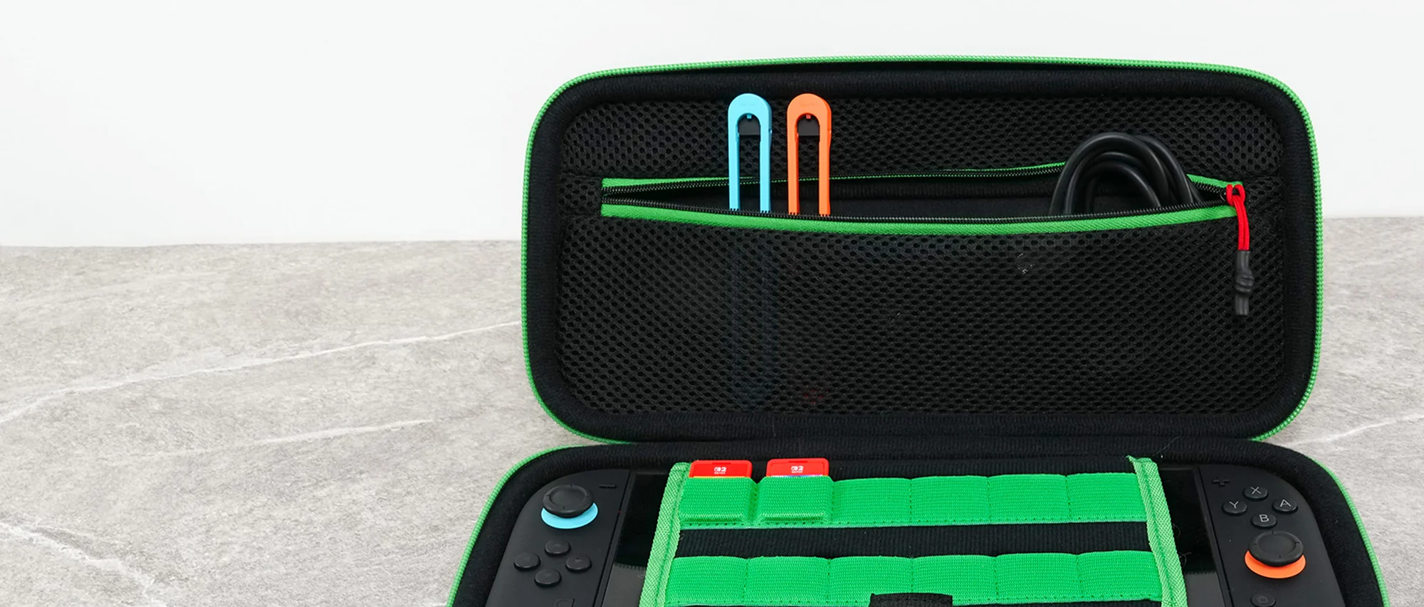 Custodia verde aperta con due controller e accessori. Strumenti di gioco blu e arancioni nella tasca.