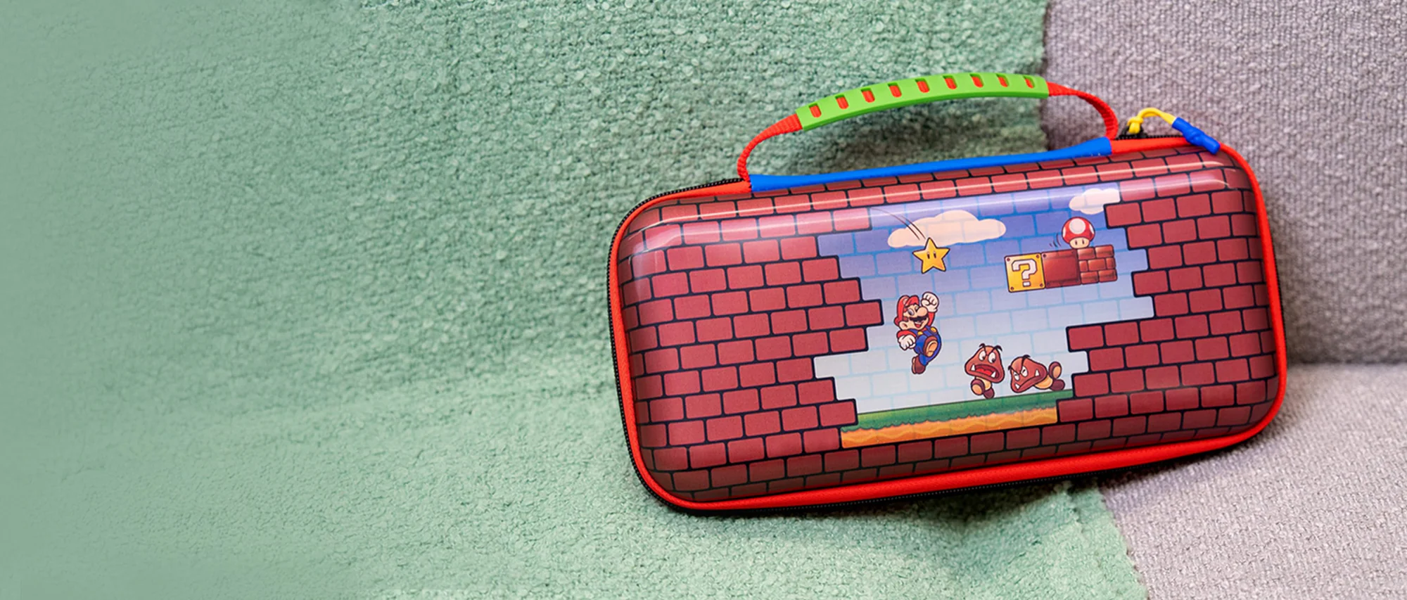 Una custodia per Nintendo Switch con una scena di Mario, su una superficie verde con un cuscino grigio a destra.