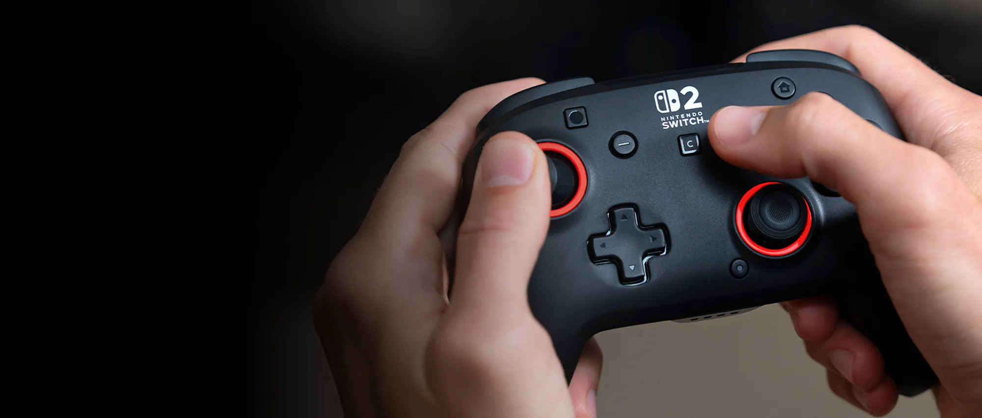 Hände halten einen schwarzen Nintendo Switch-Controller. Rote Akzente um die Joysticks. Schwarzer Hintergrund.