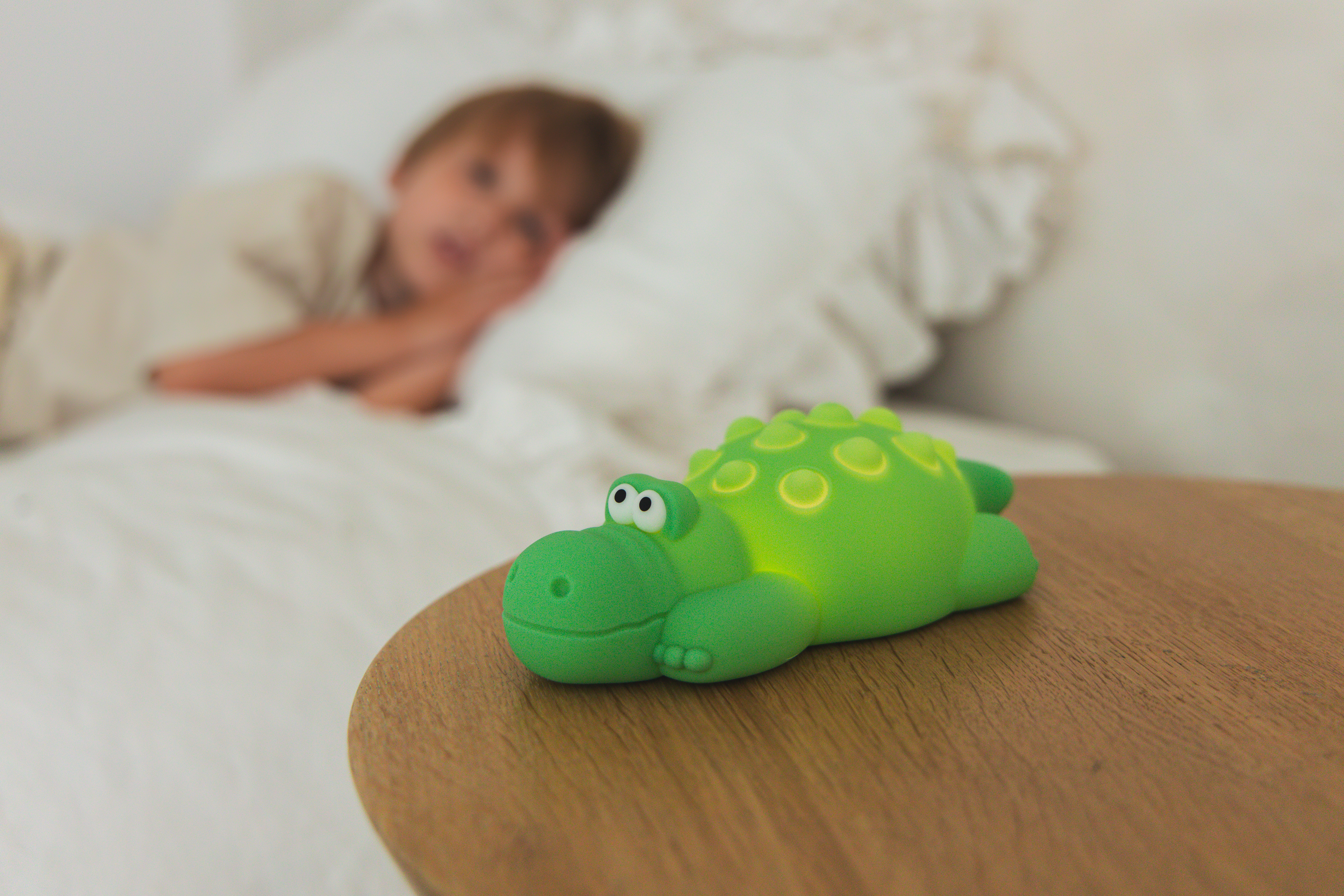 Zielona zabawka aligator na drewnianym stole. Dziecko odpoczywa na łóżku w tle, nieostre.