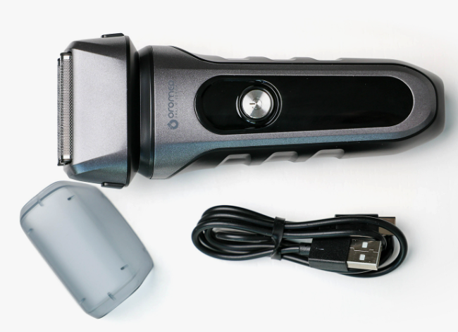 Golarka elektryczna z osłoną i kablem USB na białym tle. Golarka jest szara i czarna. Osłona jest przezroczysta.