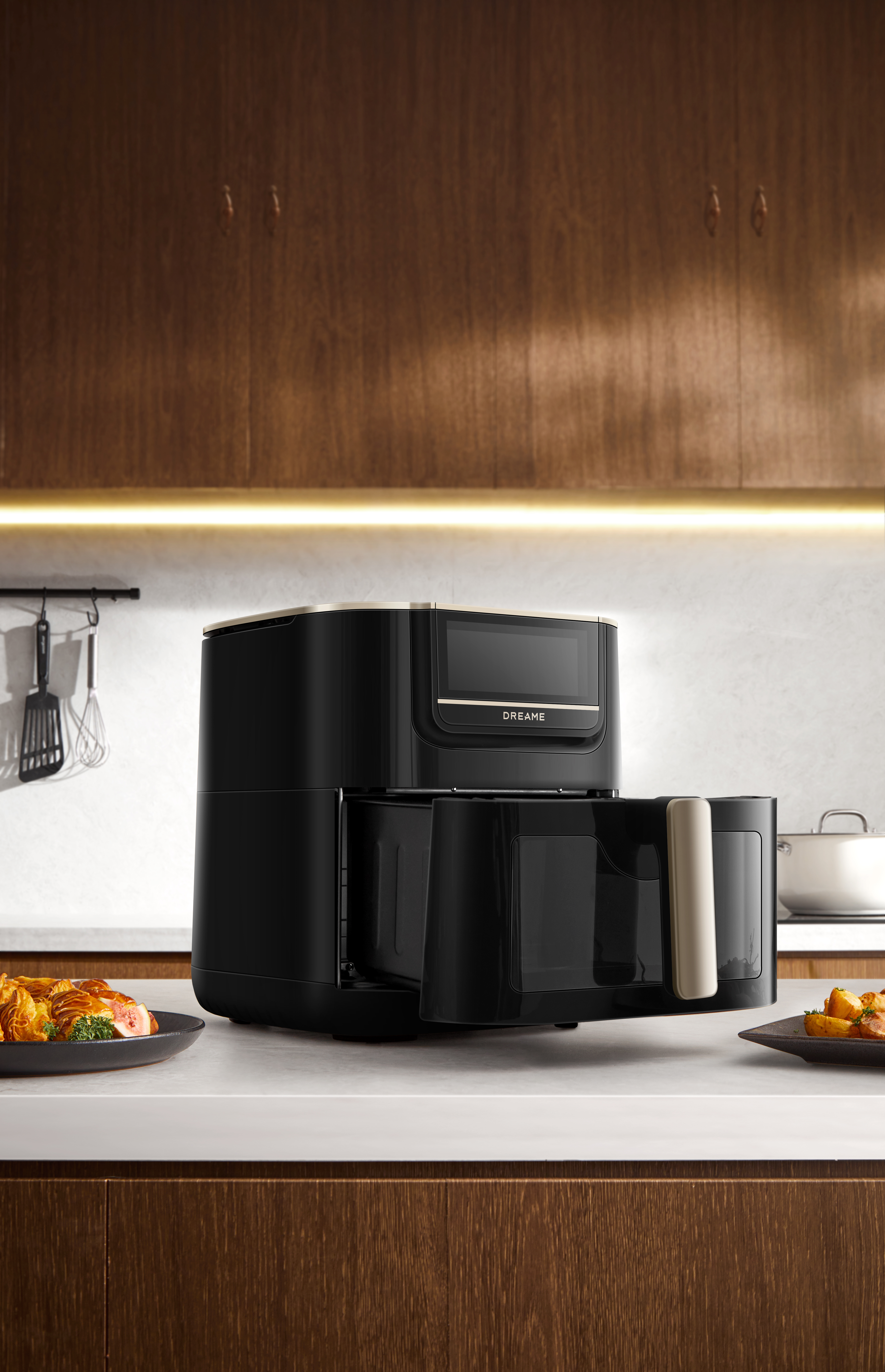 Czarna frytkownica na białym blacie, z jedzeniem na talerzach. Drewniane szafki w tle.