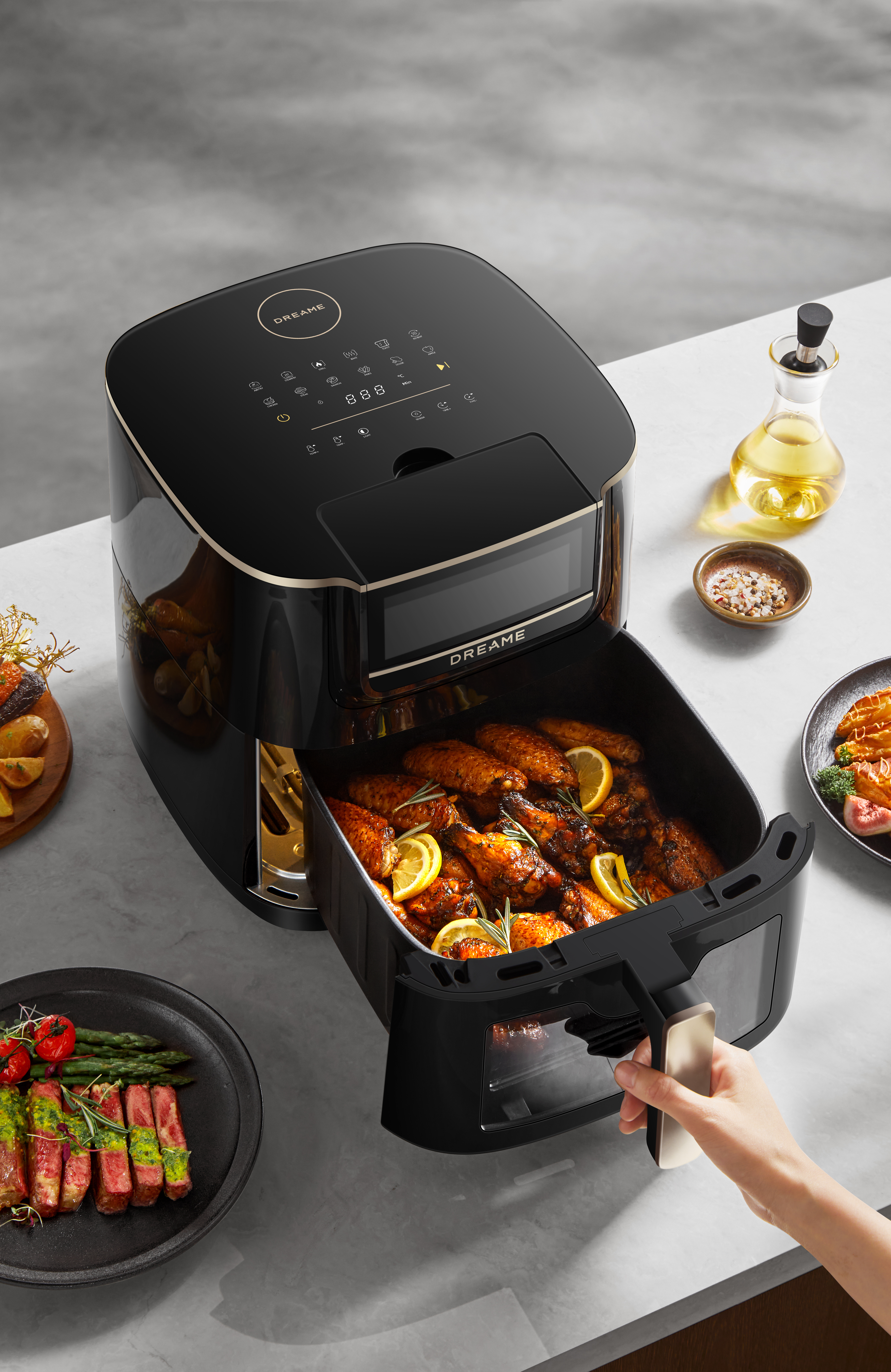 Czarna frytownica beztłuszczowa ze skrzydełkami z kurczaka, cytryną, rozmarynem. Dodatki na talerzach. Oliwa z oliwek i przyprawy.