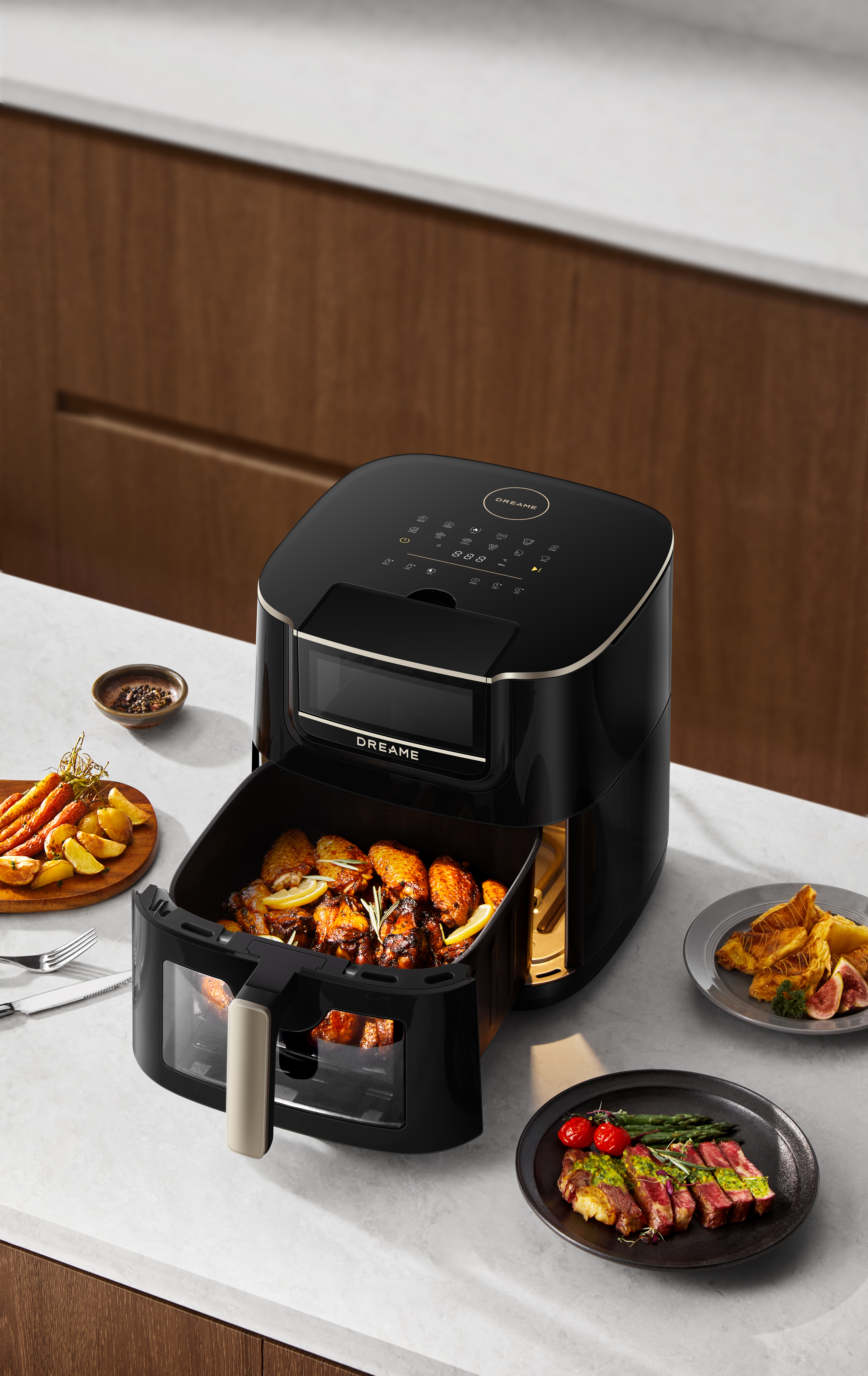 Czarna frytownica powietrzna z jedzeniem w środku, w tym kurczakiem i warzywami, na białym blacie z talerzami.
