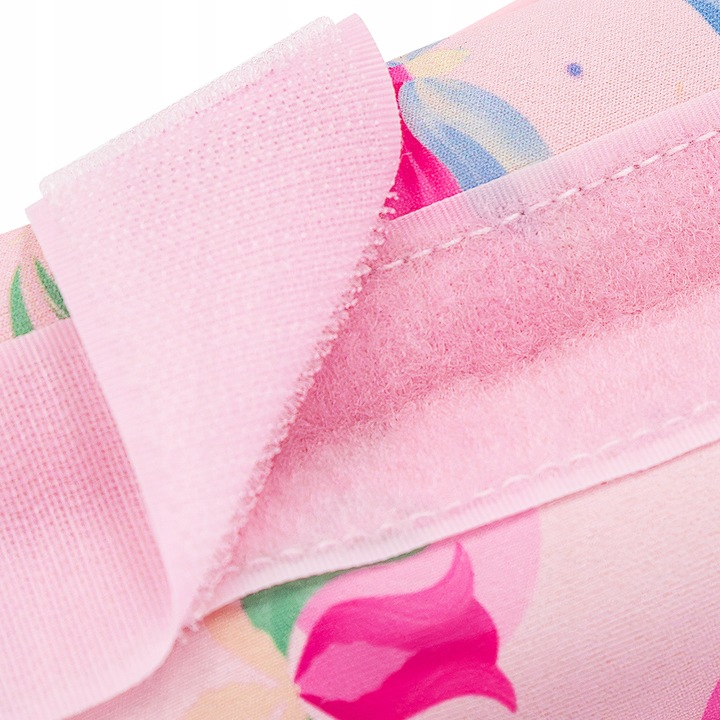 Zbliżenie różowego materiału z zapięciem na rzep. W tle widoczny wzór kwiatowy.