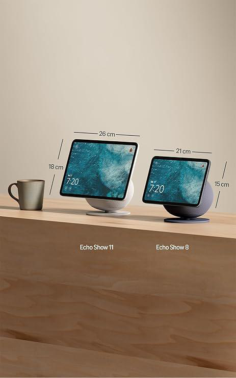 Zwei Echo Show-Geräte auf einer Holzoberfläche. Eines hat einen weißen Sockel, das andere ist dunkelgrau. Links steht eine Tasse.
