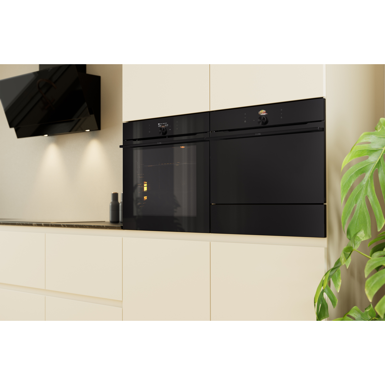 Een moderne keuken met zwarte ovens, een afzuigkap en crèmekleurige kasten. Een kamerplant rechts.
