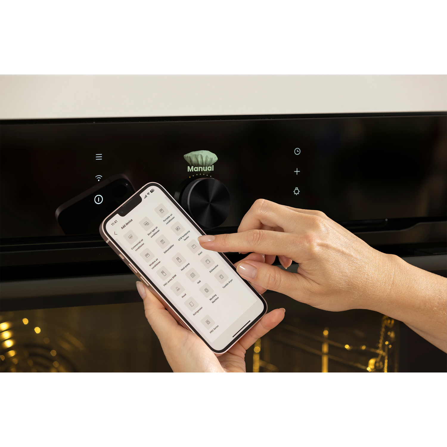Een persoon gebruikt een smartphone om een oven te bedienen. De telefoon toont pictogrammen voor diverse apparaten. De oven heeft een handmatige bediening.